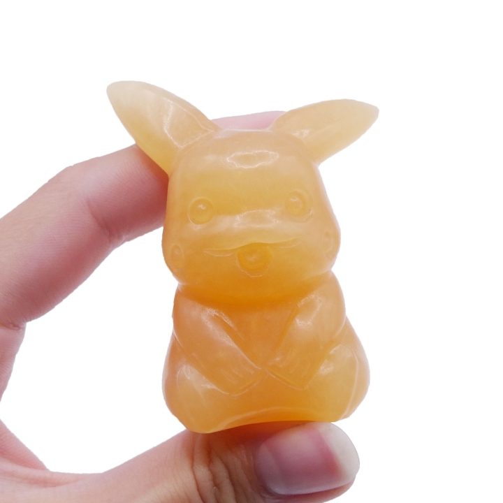 Ręcznie rzeźbiona figurka Pikachu z naturalnego, pomarańczowego kalcytu na białym tle.