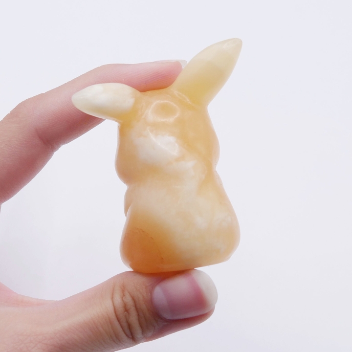 Figurka Pikachu z pomarańczowego kalcytu z widocznymi białymi przebarwieniami na białym tle.