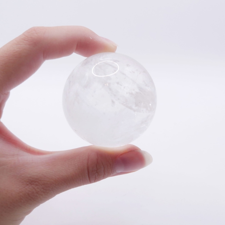 Polerowana kula z kryształu górskiego o średnicy około 45mm, na białym tle.