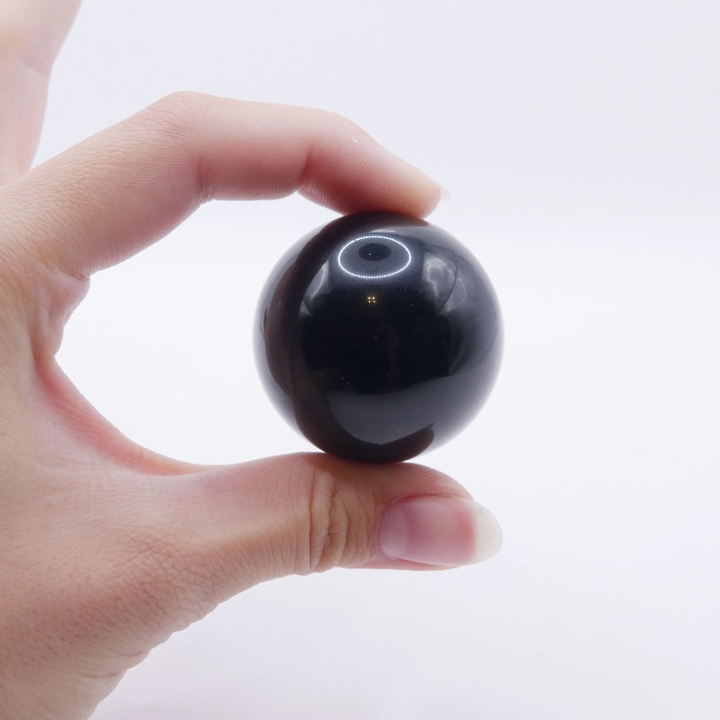 Gładka, polerowana kula z czarnego onyksu o lustrzanym połysku na białym tle.