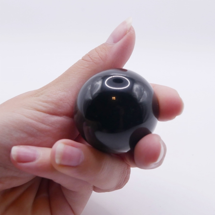 Kula z czarnego onyksu trzymana w dłoni, aby pokazać jej rozmiar i gładkość.