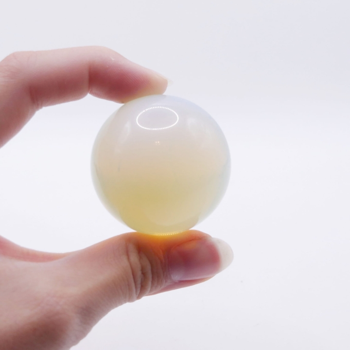 Gładka, polerowana kula z opalitu z widocznym niebieskim blaskiem wewnątrz, na białym tle.