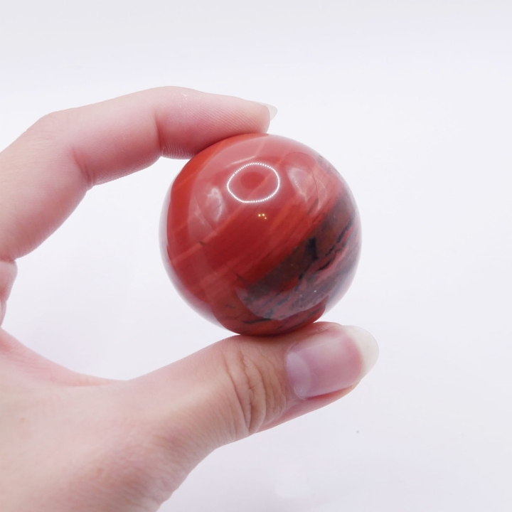 Zbliżenie na powierzchnię kuli z czerwonego jaspisu, ukazujące jej intensywną, ceglastą barwę.