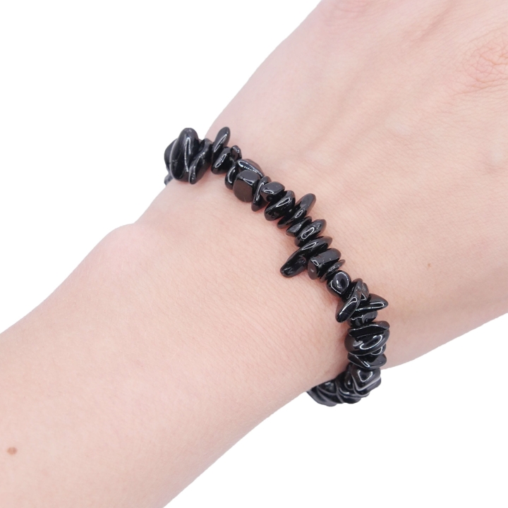 Elastyczna bransoletka z nieregularnych kawałków (sieczki) czarnego onyksu na białym tle.