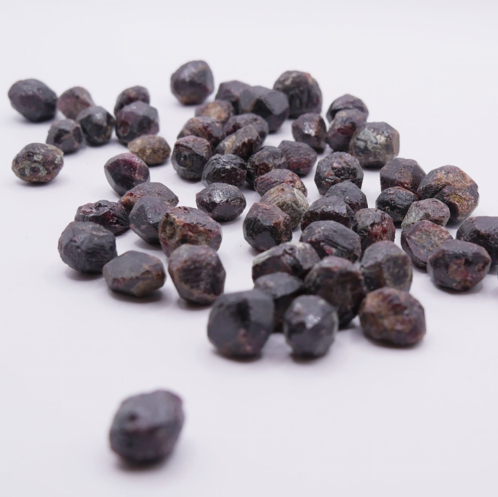 Czerwono-brązowy kamień granatu w surowej formie, trzymany w palcach.