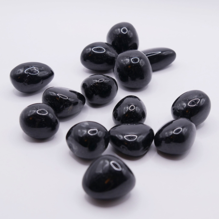 Błyszczący otoczak szerlu trzymany w palcach, ukazujący jego obły kształt.