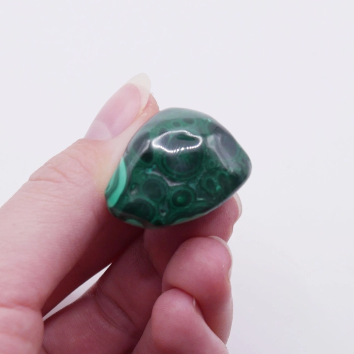 Obły kamień malachitu trzymany w dłoni, ukazujący jego kształt i połysk.