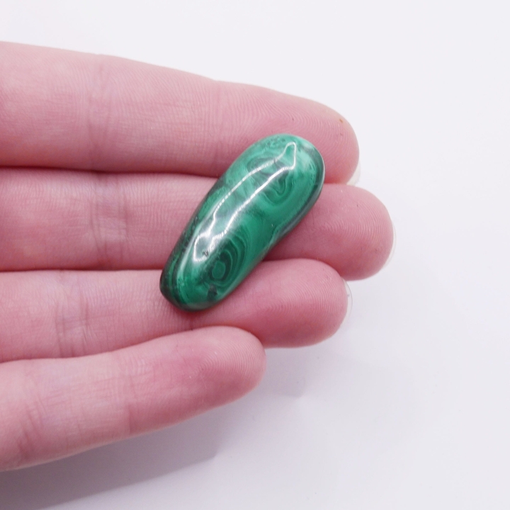 Kamień naturalny malachit o zaokrąglonym kształcie, trzymany w dłoni.