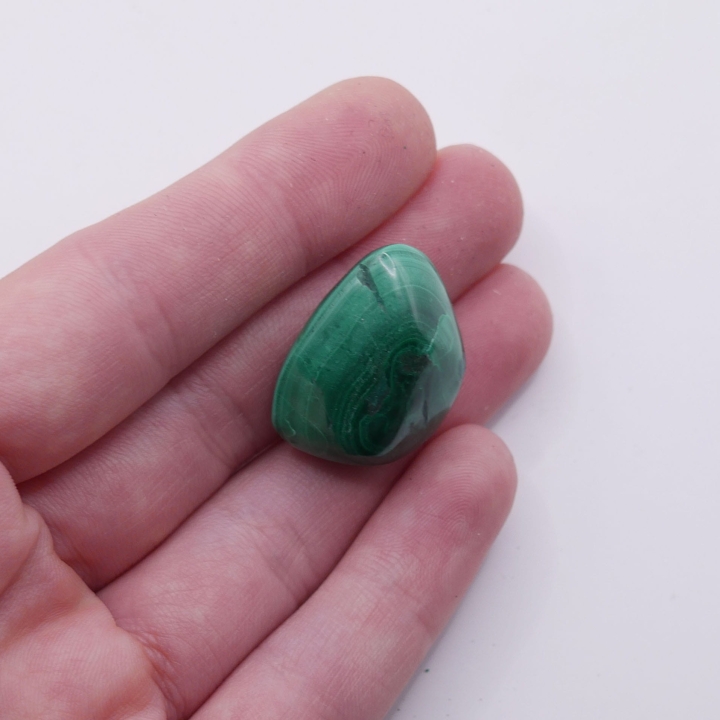 Obły otoczak z naturalnego malachitu trzymany w dłoni, ukazujący połysk.