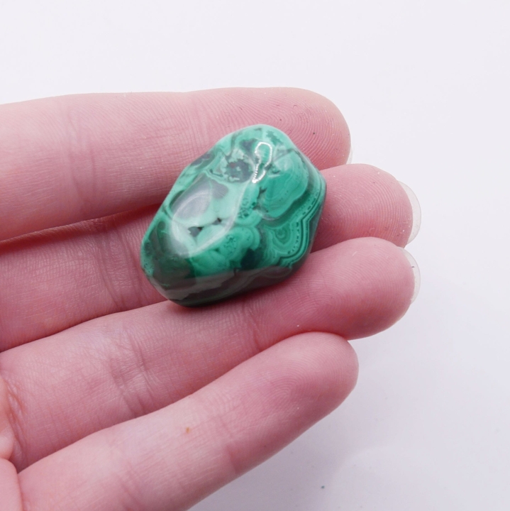 Gładki, obły malachit trzymany w dłoni, ukazujący połysk.