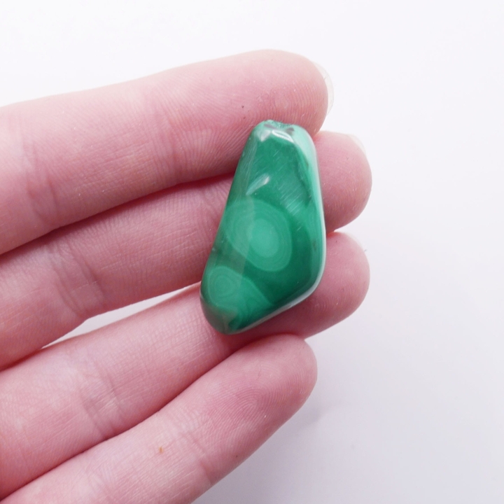 Kamień naturalny malachit o zaokrąglonym kształcie, trzymany w dłoni.