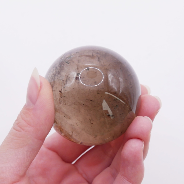 Unikatowa kula z kwarcu dymnego trzymana w dłoni, ukazująca rozmiar 52 mm.