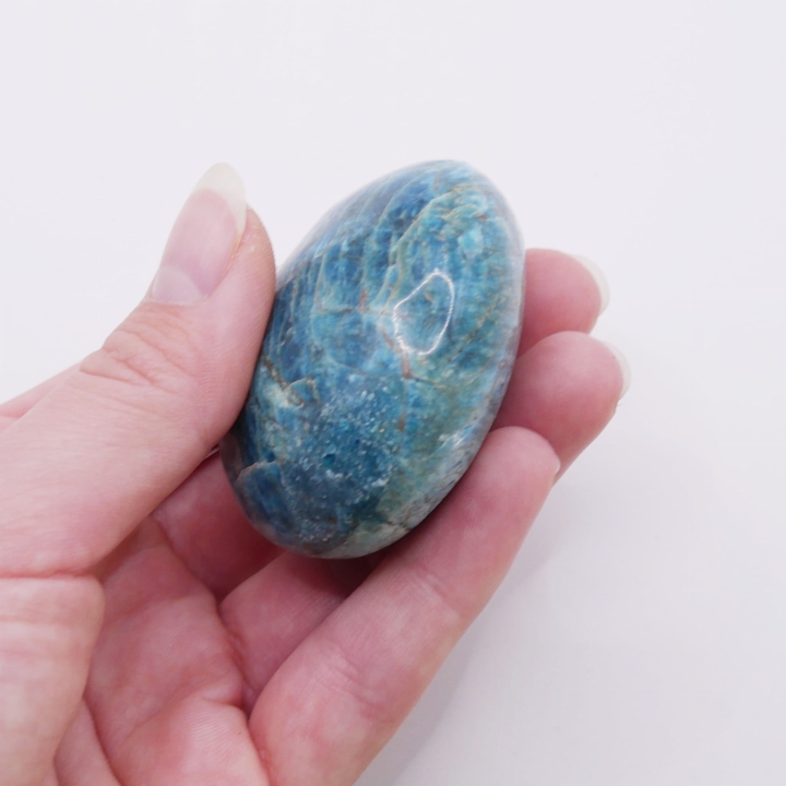 Gładki, niebieski kamień naturalny trzymany w dłoni, ukazujący połysk.