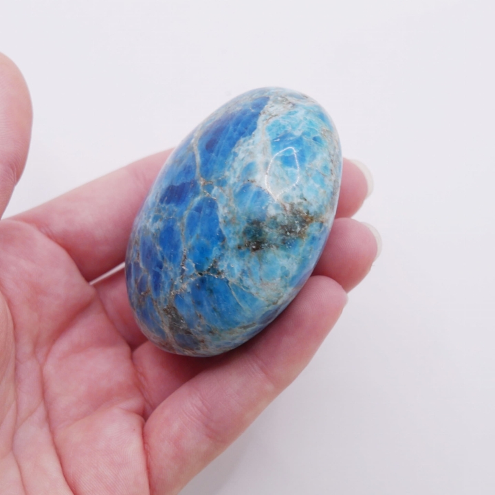 Gładki, lśniący minerał o niebieskim odcieniu trzymany w dłoni.