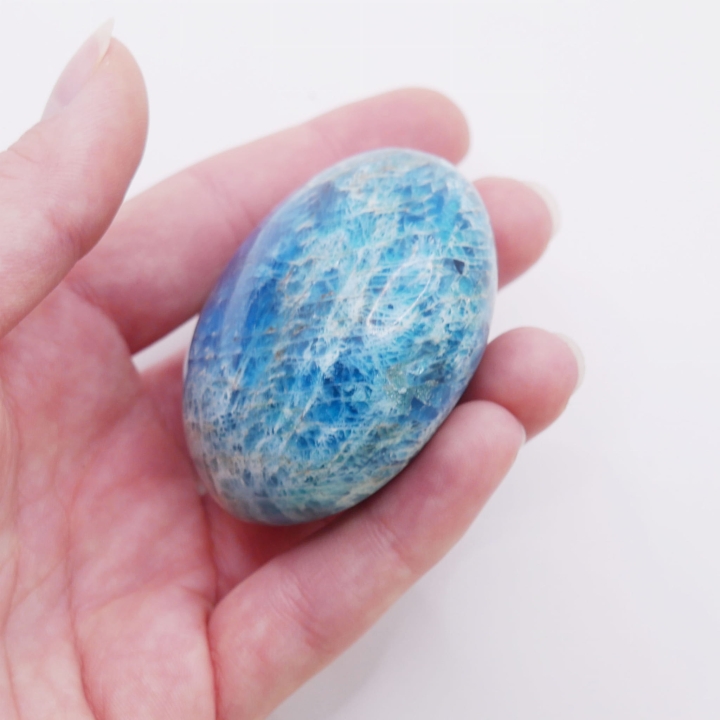 Niebiesko-zielony minerał o gładkim szlifie, trzymany w dłoni.