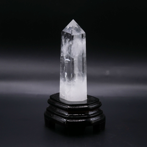 Kryształowy obelisk widok z profilu – przezroczysty okaz o szklanym połysku osadzony na drewnie.