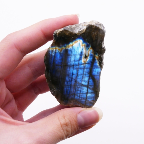 Niebiesko-złota gra barw na polerowanym froncie surowej bryłki labradorytu na białym tle.