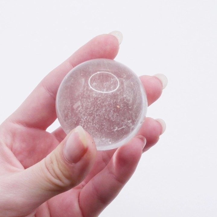 Gładka kula z kryształu górskiego trzymana w dłoni dla pokazania jej rozmiaru (ok. 43mm).